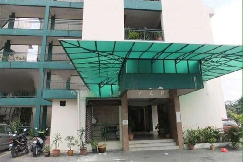 Exterior type: low-rise apartment block; features: green glass canopy, entrance with stone columns, manicured landscaping, potted plants at entrance, multiple levels visible, parking area with motorcycles, balconies with railings, exposed concrete facade; style: modern.