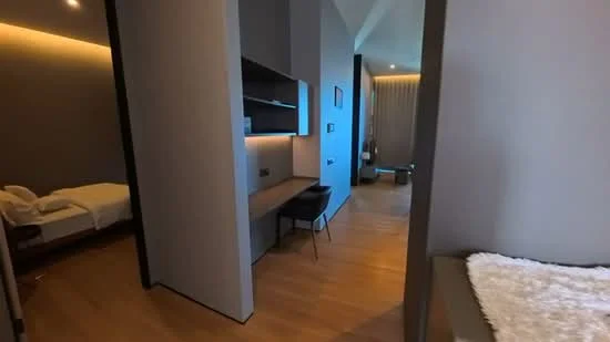 Room features: light wood flooring, grey painted walls, built-in shelving, desk with chair, recessed lighting, floor-to-ceiling windows, curtains, minimalist decor; style: modern.