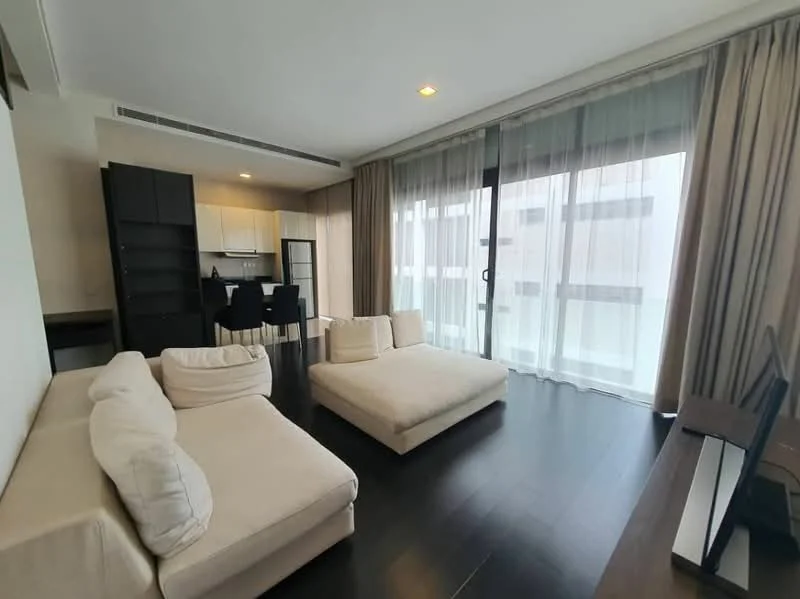 Living features: L-shape sectional sofa in cream fabric, coffee table, floor-to-ceiling windows, sheer curtains, dark wood flooring, recessed downlights, TV console, open-plan layout with kitchen, built-in shelving unit, dining area with black dining chairs; style: modern.