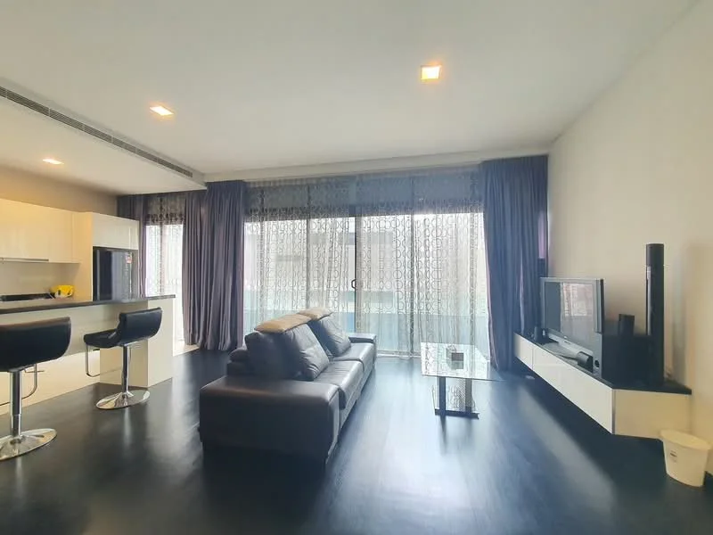 Living features: black leather sofa, glass coffee table, wall-mounted TV, white TV console, floor-to-ceiling windows, sheer curtains, dark curtains, bar stools at kitchen counter, open-plan layout, dark wood flooring, recessed downlights; style: modern; view: city.