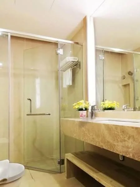 Bathroom features: glass shower enclosure, rain shower head, single-sink vanity with stone countertop, chrome basin mixer faucet, framed mirror, wooden shelving under sink, towel rack, decorative potted flowers, cream tiled walls, cream tiled flooring; style: modern.