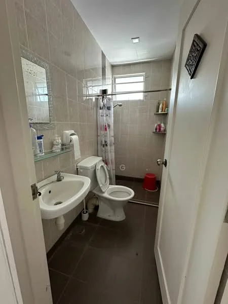 Bathroom features: grey tiled walls, brown tiled flooring, single-sink vanity with glass shelf, white toilet, shower area with curtain, mirror above sink, wall-mounted soap dispenser, toilet paper holder, small shelf with toiletries, window for natural light; style: modern.