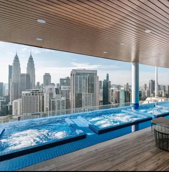 Exterior type: high-rise condominium; features: infinity pool, jacuzzi, pool deck with loungers, wooden ceiling, city skyline view, glass railing, tiled flooring, surrounded by urban landscape; style: modern.