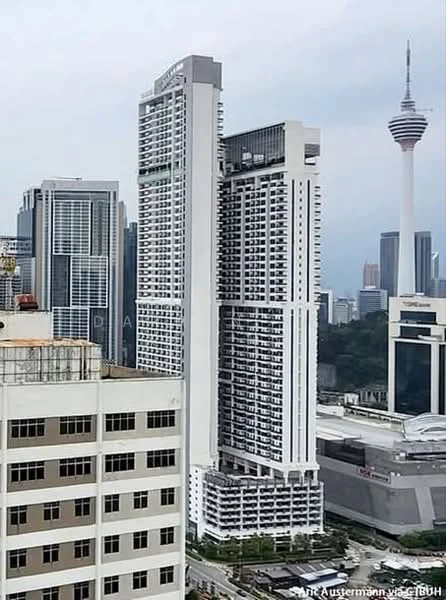 Exterior type: high-rise condominium; features: glass curtain wall, white painted facade, recessed balconies, approximately 30-storey high-rise, surrounded by urban skyline, KL Tower visible in background; style: modern.