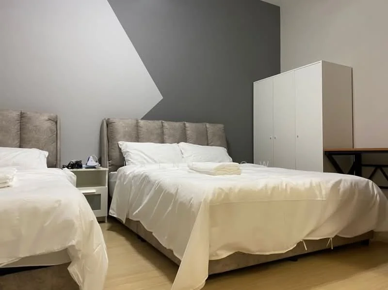 Bedroom features: two queen-size beds with upholstered headboards, white bedding, grey accent wall, light wood flooring, white bedside table, white wardrobe, wooden table, decorative wall art; style: modern.
