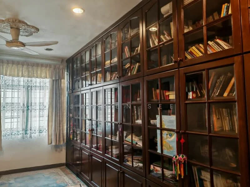 Study features: built-in wooden bookshelves with glass doors, ceiling fan, carpeted flooring, window with sheer curtains, decorative wall clock, area rug with floral pattern, wall-mounted artwork, wooden desk, multiple books and decorative items on shelves; style: traditional.