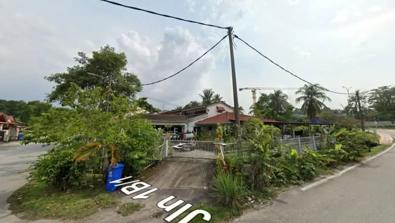 Exterior type: detached bungalow; features: red pitched tile roof, white painted facade, fenced front yard, manicured landscaping, palm trees, tropical plants, driveway with interlocking pavers, surrounded by greenery, corner lot, street view, utility pole, road access; style: traditional.