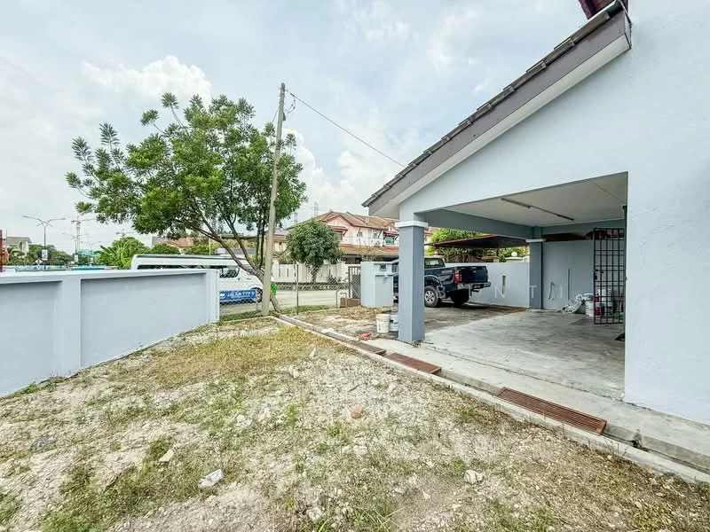 Exterior type: detached bungalow; features: single-storey building, light blue painted facade, car porch with concrete flooring, manicured lawn area, mature tree in garden, fenced perimeter, visible neighboring houses, driveway with interlocking pavers; style: modern.