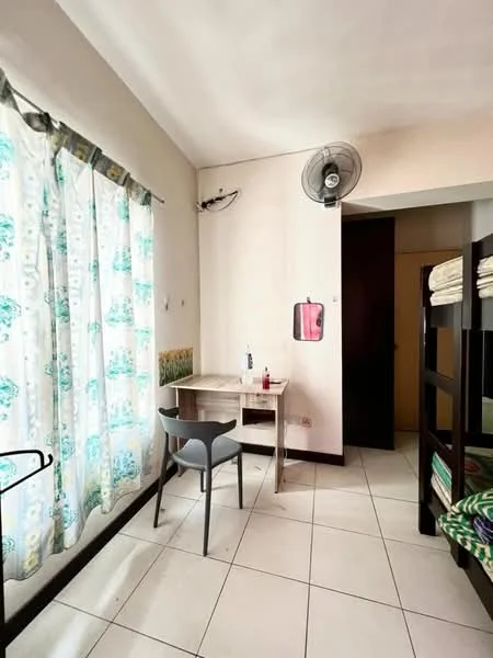 Room features: white painted walls, sloped ceiling, tiled flooring, window with sheer curtains, ceiling fan, wooden desk, plastic chair, bunk bed with green bedding, wall-mounted mirror, doorway leading to another room; style: minimalist.
