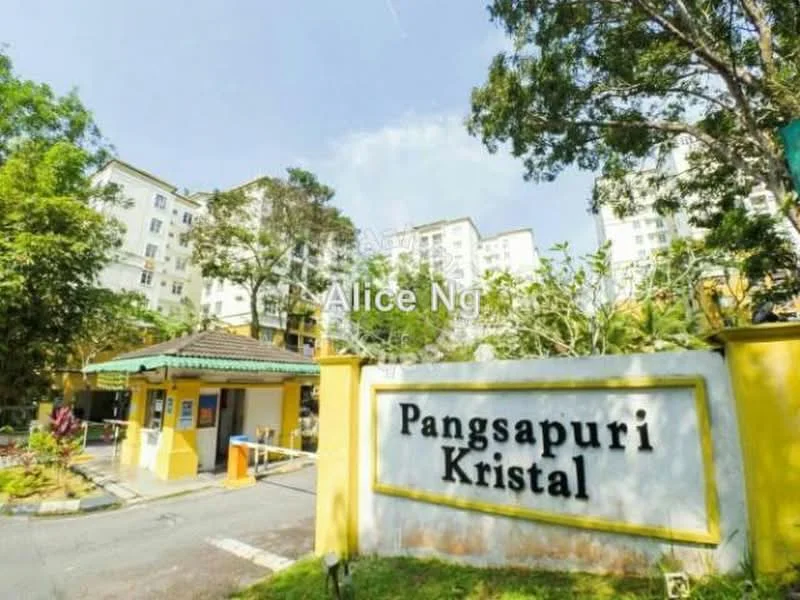 Exterior type: low-rise apartment block; features: yellow painted facade, green roof awning, manicured landscaping, paved driveway, security guard house at entrance, surrounded by mature trees, signage with 'Pangsapuri Kristal', multiple storeys visible in background; style: modern.