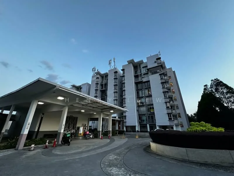 Exterior type: mid-rise condominium; features: grey painted facade, balconies on upper floors, multiple antennas on roof, covered entrance with awning, driveway leading to entrance, landscaped garden area, security checkpoint, visible parking area; style: modern.