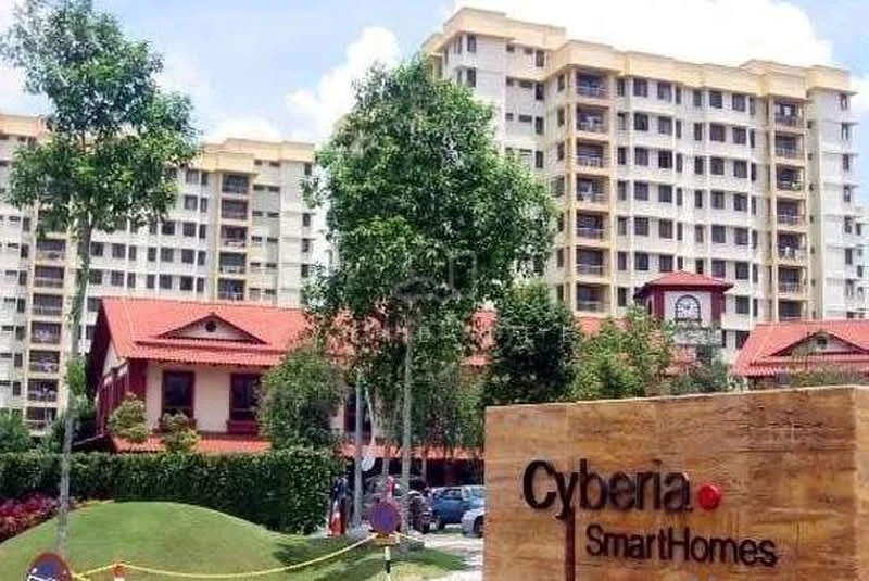 Exterior type: low-rise apartment block; features: cream painted facade, red tiled roof, landscaped garden with manicured lawn, mature trees, signage with 'Cyberia SmartHomes', multiple storeys, surrounded by greenery, parking area visible; style: modern.