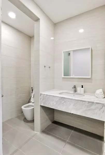 Bathroom features: marble countertop, single-sink vanity, framed mirror, one-piece toilet, grey ceramic tile flooring, white tiled walls, recessed lighting, wall-mounted faucet; style: modern.