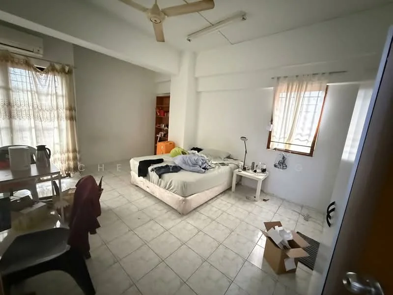 Bedroom features: queen-size bed with bedding, wooden bedside table, desk lamp, floor-to-ceiling window with sheer curtains, wall-mounted air conditioning unit, ceiling fan, tile flooring, light-colored walls, clothes on chair, cardboard boxes, dining table with chairs visible in background.