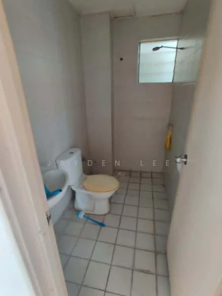 Bathroom features: white ceramic toilet, single-sink vanity, mirror above sink, shower area with glass partition, tile flooring, grey wall tiles, window for natural light, yellow towel hanging, blue cleaning supplies, light fixture on ceiling.