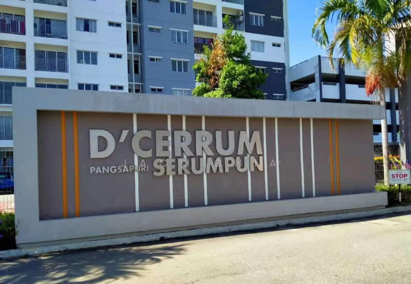 Exterior type: low-rise apartment block; features: signage with name 'D'CERRUM SERUMPUN', grey painted facade, landscaped area with palm trees, surrounding residential buildings, paved driveway, stop sign visible; style: modern.
