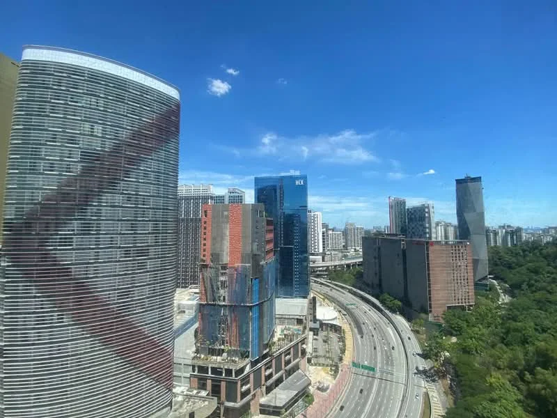 Exterior type: high-rise condominium; features: glass curtain wall, concrete facade, surrounded by urban development, view of highway, city skyline in background, greenery along the roadside; style: modern.