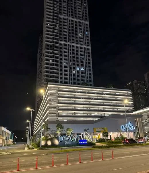 Exterior type: high-rise condominium; features: glass curtain wall, illuminated signage, multiple balconies, modern facade with horizontal lines, landscaped entrance, surrounded by street lighting, open-air parking area, urban context with nearby buildings; style: modern.