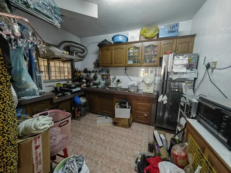 Kitchen features: brown wooden cabinetry, white tiled walls, pink vinyl flooring, stainless-steel fridge, built-in oven, microwave, toaster, coffee machine, sink, countertop with clutter, various kitchen utensils, laundry basket, boxes and bags on the floor.