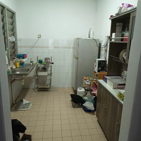 Kitchen features: single-bowl stainless-steel sink, chrome pull-down faucet, white tiled backsplash, white wall tiles, light brown laminate cabinetry, built-in refrigerator, countertop with clutter, floor tiles in beige, open shelving, kitchen cart, various kitchen appliances, garbage bag on floor.