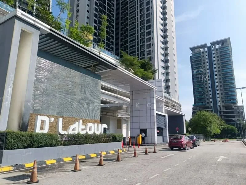 Exterior type: high-rise condominium; features: modern facade with glass and concrete, landscaped entrance with greenery, prominent signage with 'D'Latour', multiple storeys visible, open-air parking area, surrounding mature trees, paved driveway, security cones along the road; style: modern.