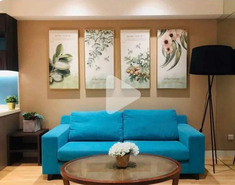Living features: turquoise fabric sofa, round wooden coffee table, framed botanical artwork on walls, decorative flower arrangement on table, lampshade floor lamp, light wood flooring, cream painted walls, built-in cabinetry with blue lighting; style: modern.