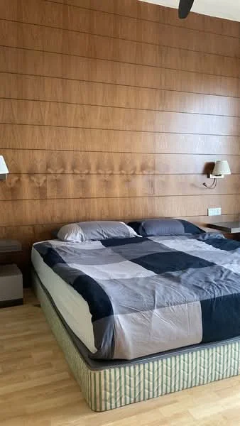 Bedroom features: king-size bed, upholstered headboard, plaid bedding, wood panel accent wall, two wall-mounted sconces, laminate flooring, nightstands on either side, light-colored bedding; style: modern.