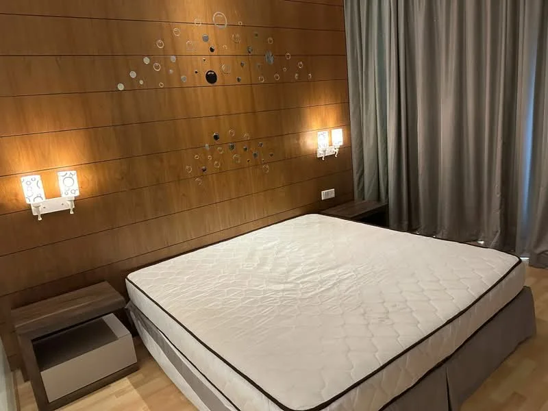 Bedroom features: wood panelled accent wall, grey curtains, queen-size bed frame, nightstands with drawers, lamps on nightstands, wooden flooring, decorative wall art, no mattress on bed; style: modern.