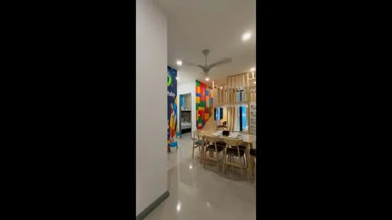 Room features: white painted walls, colourful accent wall, ceiling fan, marble flooring, dining table with chairs, wooden partition, bright lighting, decorative wall art; style: modern.