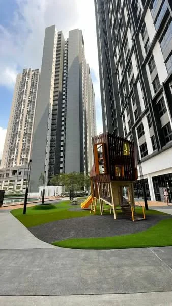 Exterior type: high-rise condominium; features: playground with wooden play structure, slide, artificial grass, concrete walkway, surrounding high-rise buildings, landscaped area, outdoor lighting, swimming pool visible in background; style: modern.