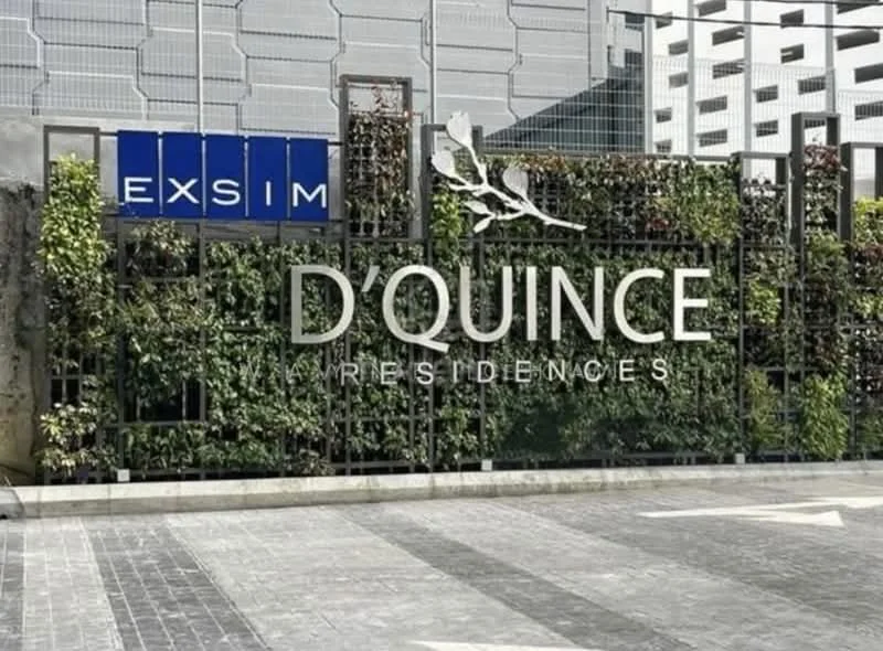 Exterior features: modern facade, green wall with plants, signage with 'D'QUINCE RESIDENCES', paved walkway, surrounding parking structure, glass panels, metal fencing; style: modern.