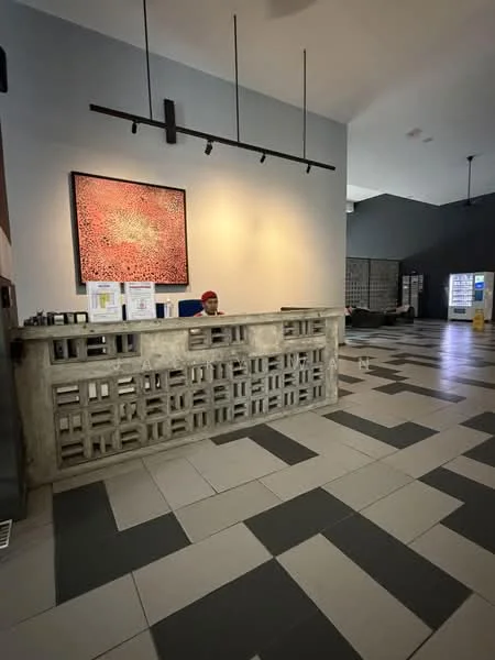 Room features: reception desk with decorative concrete block design, grey painted walls, large artwork on wall, track lighting, tiled flooring with black and white pattern, seating area with chairs, vending machine, information board, open space layout; style: modern.