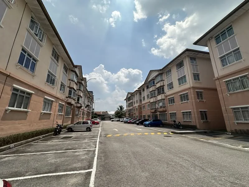 Exterior type: low-rise apartment block; features: two-storey building, cream painted facade, balconies with railings, parking lot with marked spaces, landscaped greenery along the building, surrounded by open space, multiple vehicles parked, cloudy sky with sunlight; style: modern.