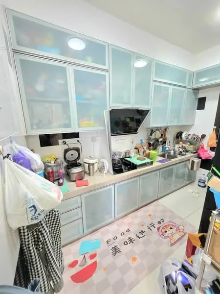 Kitchen features: light blue glass-front upper cabinets, white lower cabinets, laminate countertop, stainless-steel sink, chrome pull-down faucet, built-in oven, freestanding range oven, microwave, coffee machine, toaster, various kitchen utensils and appliances, area rug with food-themed design, white tiled flooring, recessed ceiling lights; style: modern.