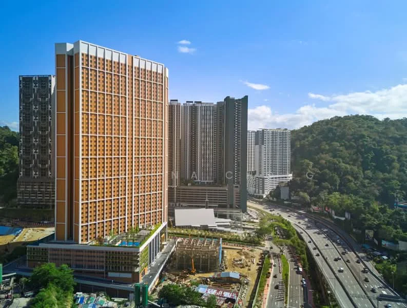 Exterior type: high-rise condominium; features: orange and grey facade, glass curtain wall, multiple balconies, surrounded by greenery, adjacent to highway, manicured landscaping, construction site in foreground; style: modern.