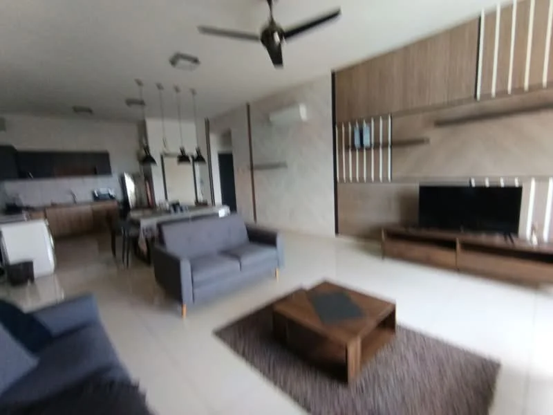 Living features: 3-seater fabric sofa in grey, 2-seater fabric sofa in navy blue, wooden coffee table, area rug with geometric pattern, wall-mounted TV, TV console, ceiling fan with light, recessed downlights, wall paneling with shelves, cream painted walls, tile flooring, open layout to kitchen, large windows for natural light; style: modern.