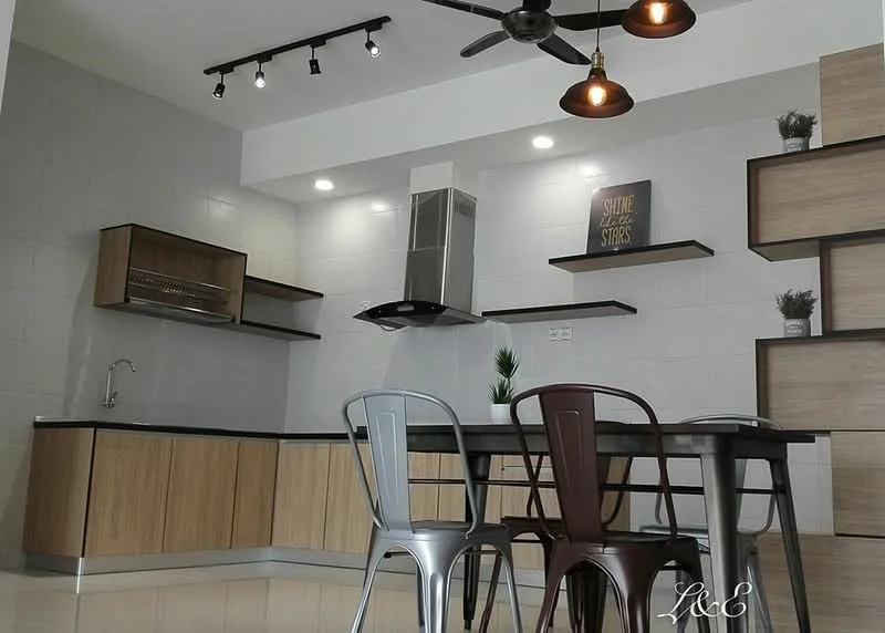 Kitchen features: grey painted walls, white ceiling, recessed LED downlights, 5-blade ceiling fan with light, black countertop, wood cabinetry with light wood finish, stainless-steel range hood, open shelving, kitchen island with seating, metal dining table, metal chairs in silver and black, decorative plant on shelf, framed wall art; style: modern.