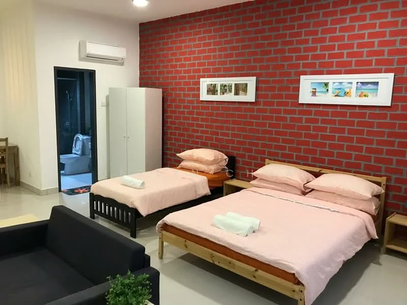Bedroom features: two single beds with pink bedding, double bed with pink bedding, white pillows, exposed red brick accent wall, cream painted walls, polished tile flooring, 1 wall-mounted split AC, framed artwork on wall, black wooden bed frames, black sofa, white wardrobe, decorative plant on table; style: modern. Bathroom features: toilet visible through doorway.