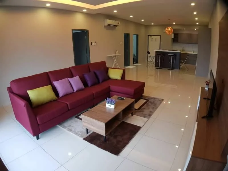 Living features: 3-seater fabric sofa in red, decorative cushions in purple and yellow, coffee table in wood, area rug in brown, wall-mounted TV, TV console in wood, recessed downlights, ceiling with tray design, white tiled flooring, air conditioning unit on wall, open layout to kitchen, decorative plant on coffee table; style: modern. Kitchen features: kitchen island with bar stools, stainless-steel appliances, grey cabinetry, white countertop, open layout to living area; style: modern.