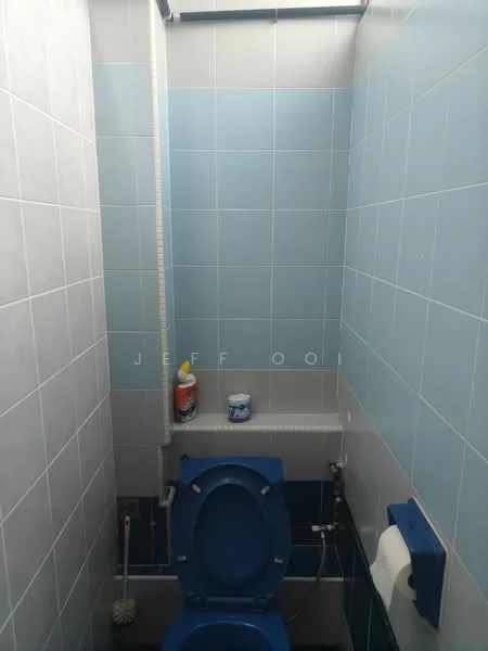 Bathroom features: blue toilet, white toilet paper holder, white wall tiles, light blue wall tiles, cleaning supplies on shelf, sink with faucet, mirror above sink, shower hose, floor tiles, toilet brush holder.