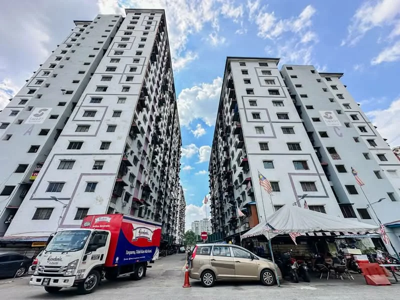 Exterior type: mid-rise condominium; features: grey painted facade, multiple storeys, balconies on each floor, visible windows, parking area in front, tents for outdoor activities, surrounding greenery, flag poles with flags, clear blue sky, clouds in the sky; style: modern.