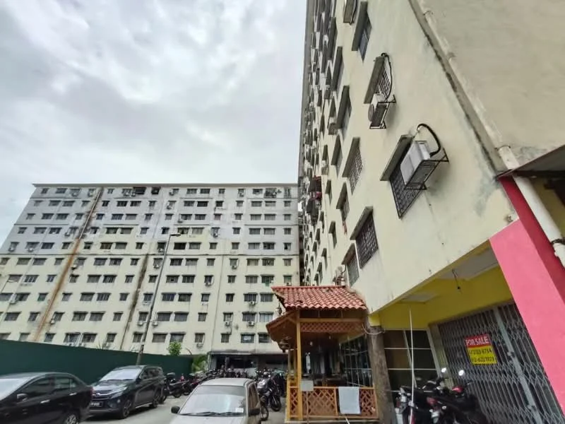Exterior type: low-rise apartment block; features: cream painted facade, multiple air conditioning units, balconies with metal railings, ground-level parking area, surrounding vehicles, two adjacent buildings, roof with decorative tiles, signage visible on the building; style: modern.