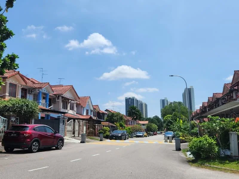 Exterior type: linked terrace house; features: red tiled roof, two-storey houses, manicured lawns, paved driveway, street lighting, surrounding greenery, blue sky, urban context with high-rise buildings in background; style: traditional.