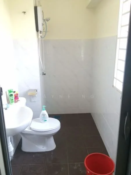 Bathroom features: white toilet, shower with wall-mounted water heater, white sink, brown tiled flooring, white wall tiles, grey accent wall tiles, toilet paper holder, cleaning supplies on shelf, red bucket.