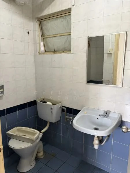 Bathroom features: white tiled walls, blue tiled flooring, toilet, sink with faucet, mirror, window, exposed plumbing, wall-mounted soap dispenser.