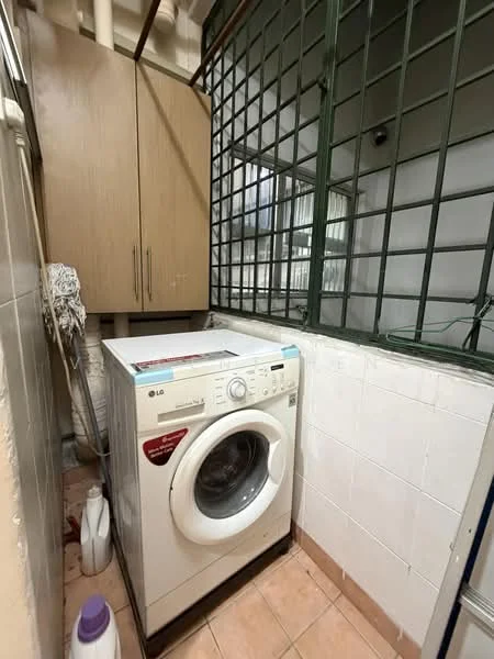 Laundry features: front-load washing machine, wooden cabinetry, white tiled walls, pink tiled flooring, window with metal grille, laundry detergent bottle, cleaning mop, corner layout.