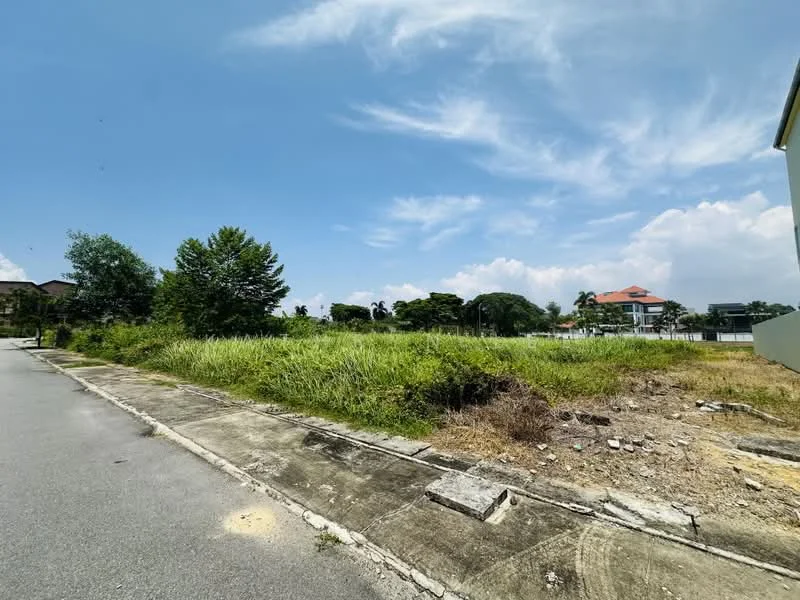 Exterior features: vacant land, overgrown grass, paved road, sidewalk, surrounding trees, clear blue sky, distant residential buildings.