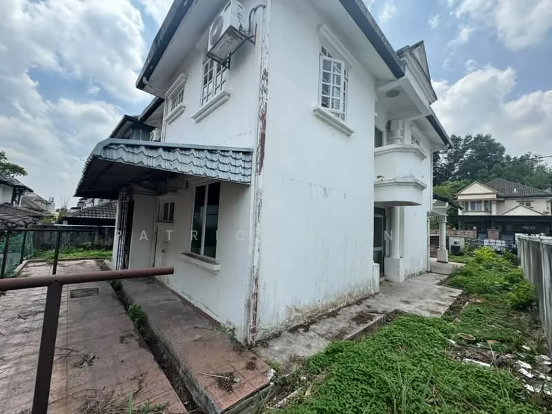 Exterior type: detached bungalow; features: white painted facade, pitched tile roof, single-storey, surrounded by overgrown grass, patio area with concrete flooring, visible air conditioning unit, gutter along the roof edge, windows with grid pattern, fenced yard, adjacent residential buildings in background; style: traditional.