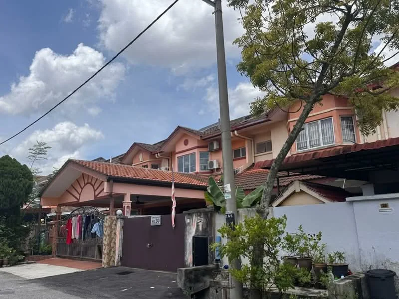 Exterior type: linked terrace house; features: pink painted facade, pitched tile roof, two-storey building, front porch with car access, decorative wooden elements on facade, visible air conditioning units, manicured garden area, flagpole with flag, laundry hanging on the porch, surrounded by greenery; style: traditional.