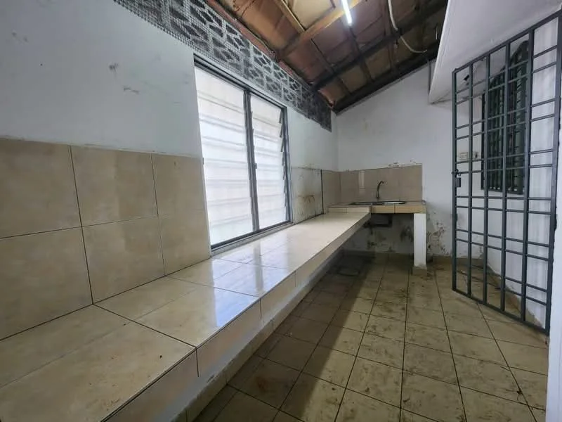 Kitchen features: long tiled countertop, single-bowl stainless-steel sink, wall-mounted faucet, large window with metal bars, cream tiled walls, brown tiled flooring, exposed ceiling with beams, no cabinetry, minimal lighting.